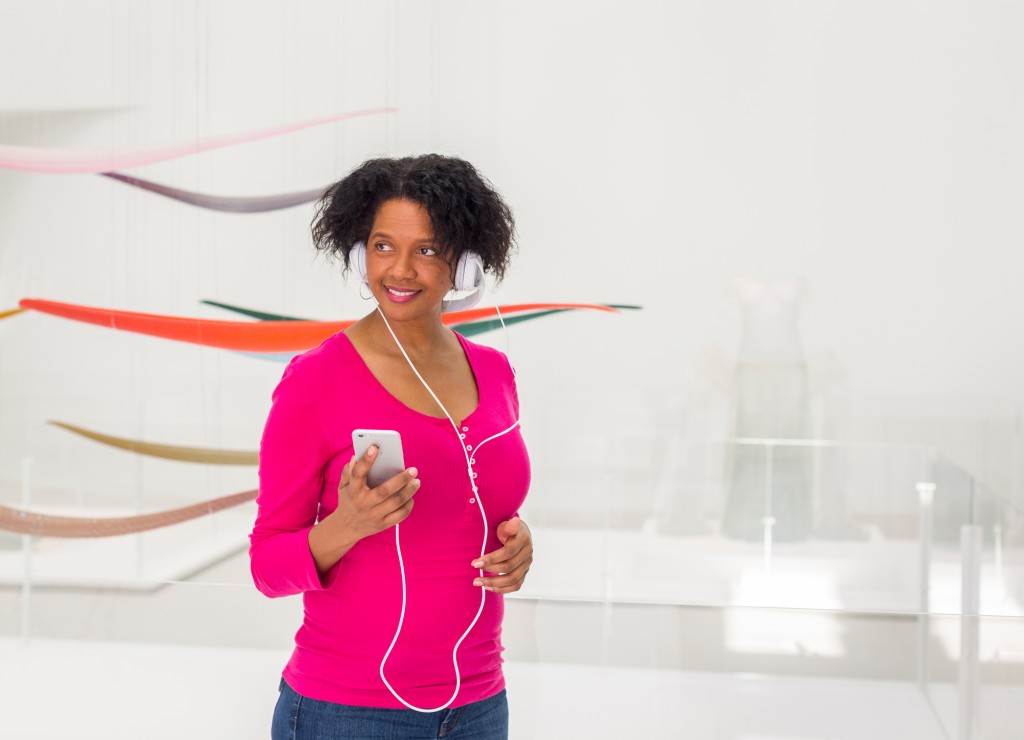 A woman stands in a museum gallery with her mobile phone and headphones